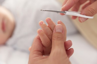 Photo of Mother cutting her cute little baby's nails on bed, closeup