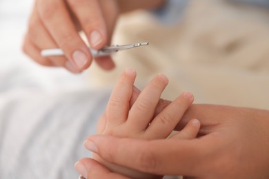 Photo of Mother cutting her cute little baby's nails on bed, closeup