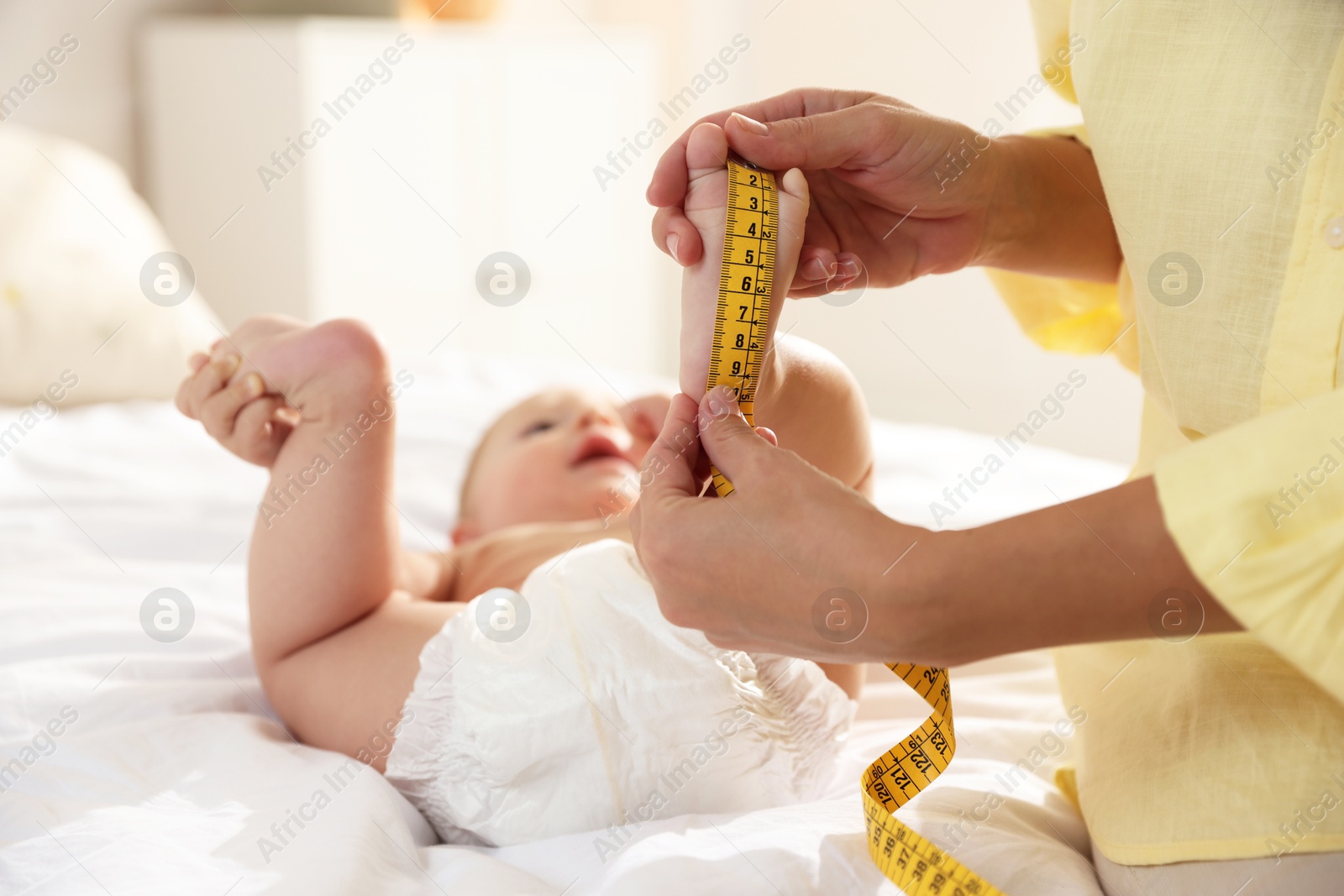 Photo of Mother measuring little baby's foot on bed, closeup