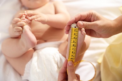 Photo of Mother measuring little baby's foot on bed, selective focus