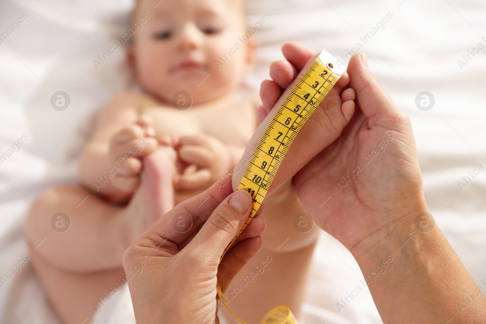 Photo of Mother measuring little baby's foot on bed, selective focus