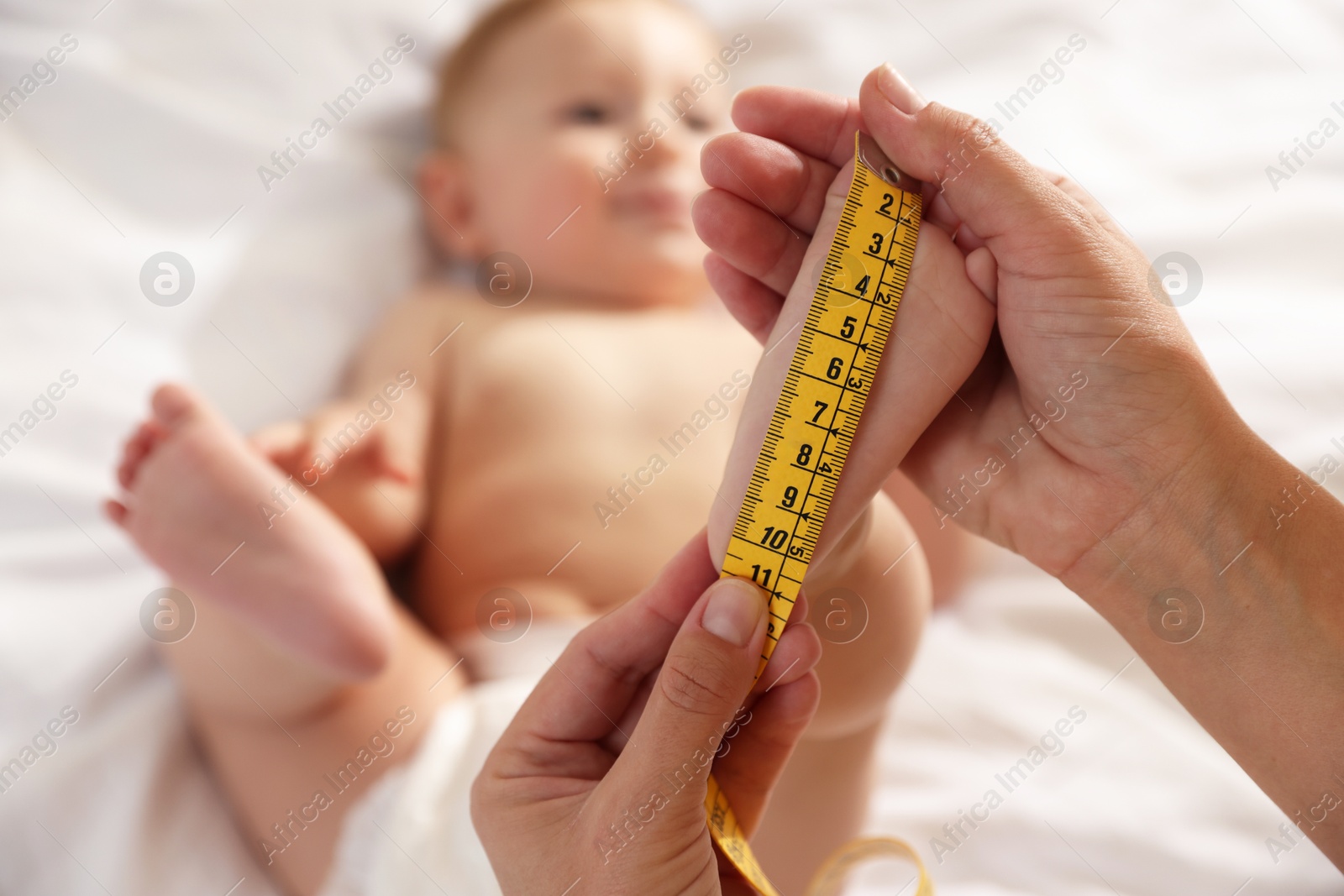 Photo of Mother measuring little baby's foot on bed, selective focus