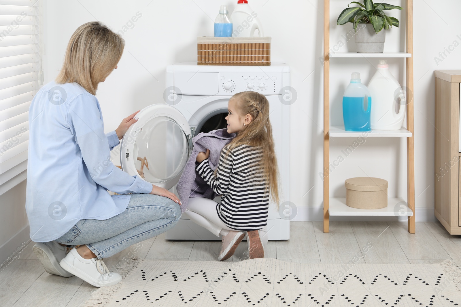 Photo of Little girl helping her mom doing laundry at home