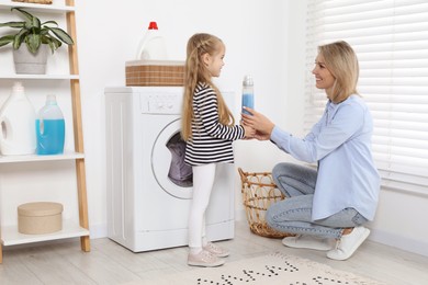 Photo of Little girl with detergent helping her mom doing laundry at home