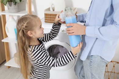 Photo of Little girl with detergent helping her mom doing laundry at home