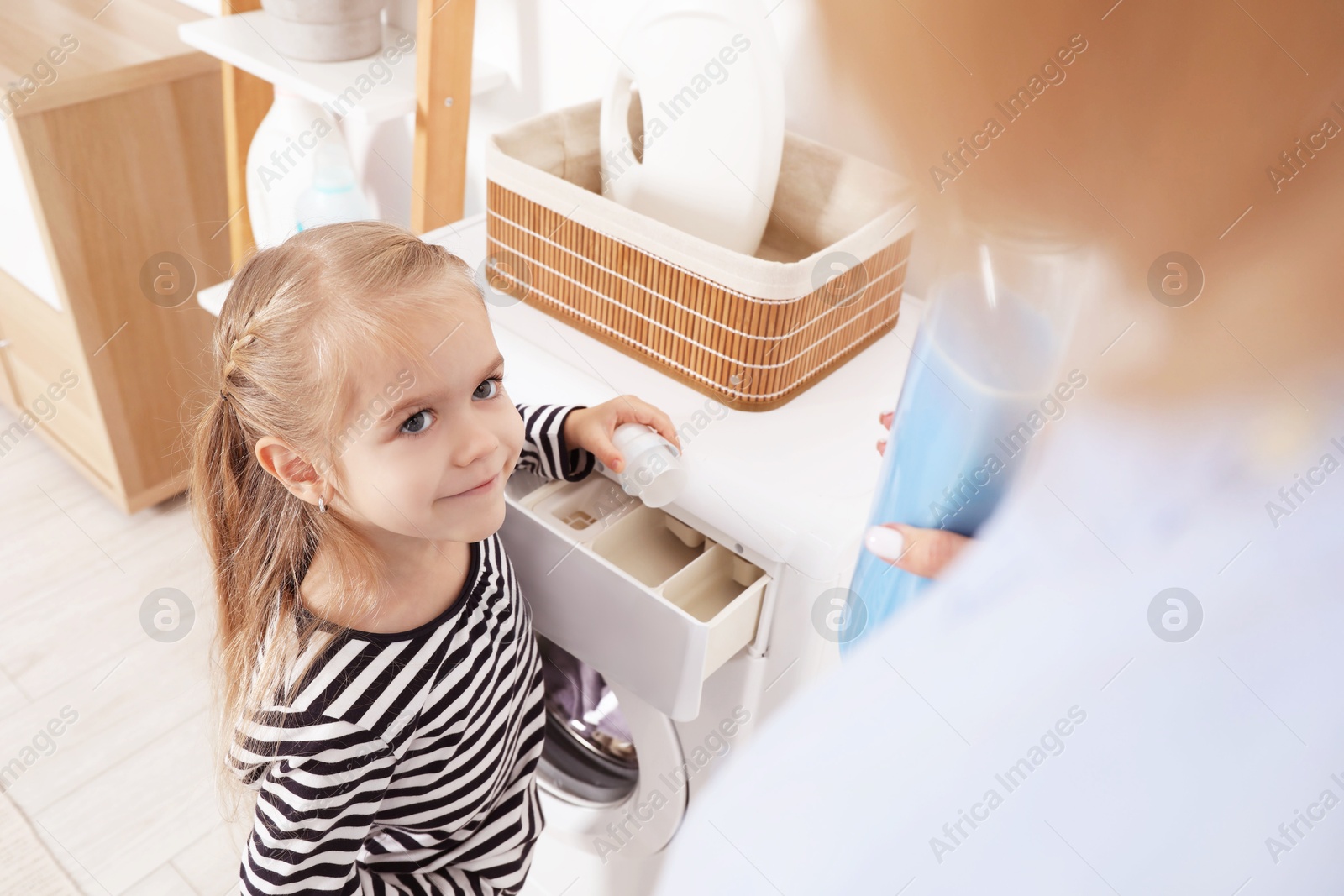 Photo of Little girl with detergent helping her mom doing laundry at home