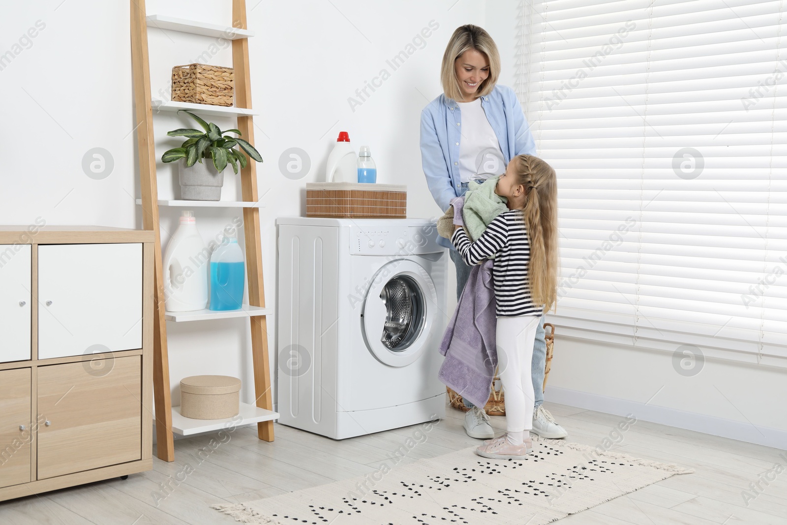 Photo of Little girl helping her mom doing laundry at home