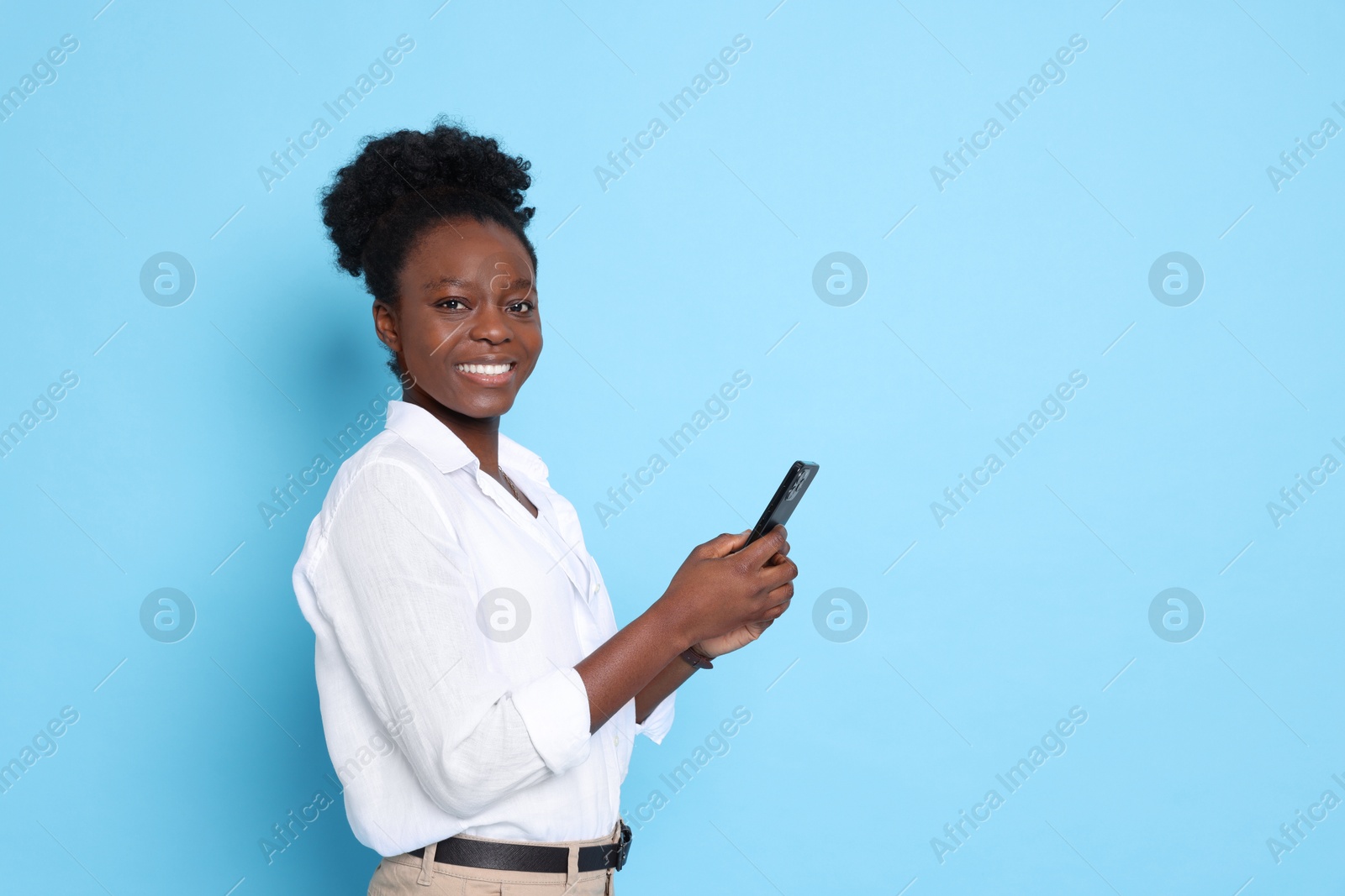 Photo of Happy woman with smartphone on light blue background. Space for text