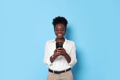 Happy woman with smartphone on light blue background. Space for text