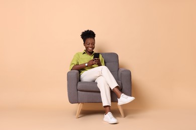 Photo of Smiling woman with smartphone sitting in armchair on beige background