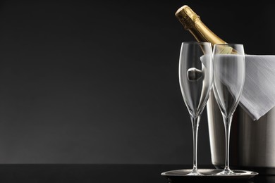 Photo of Bottle of sparkling wine in cooler bucket and glasses on black table against grey background. Space for text