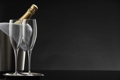 Photo of Bottle of sparkling wine in cooler bucket and glasses on black table against grey background. Space for text