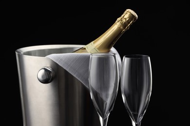 Photo of Bottle of sparkling wine in cooler bucket and glasses against black background, closeup