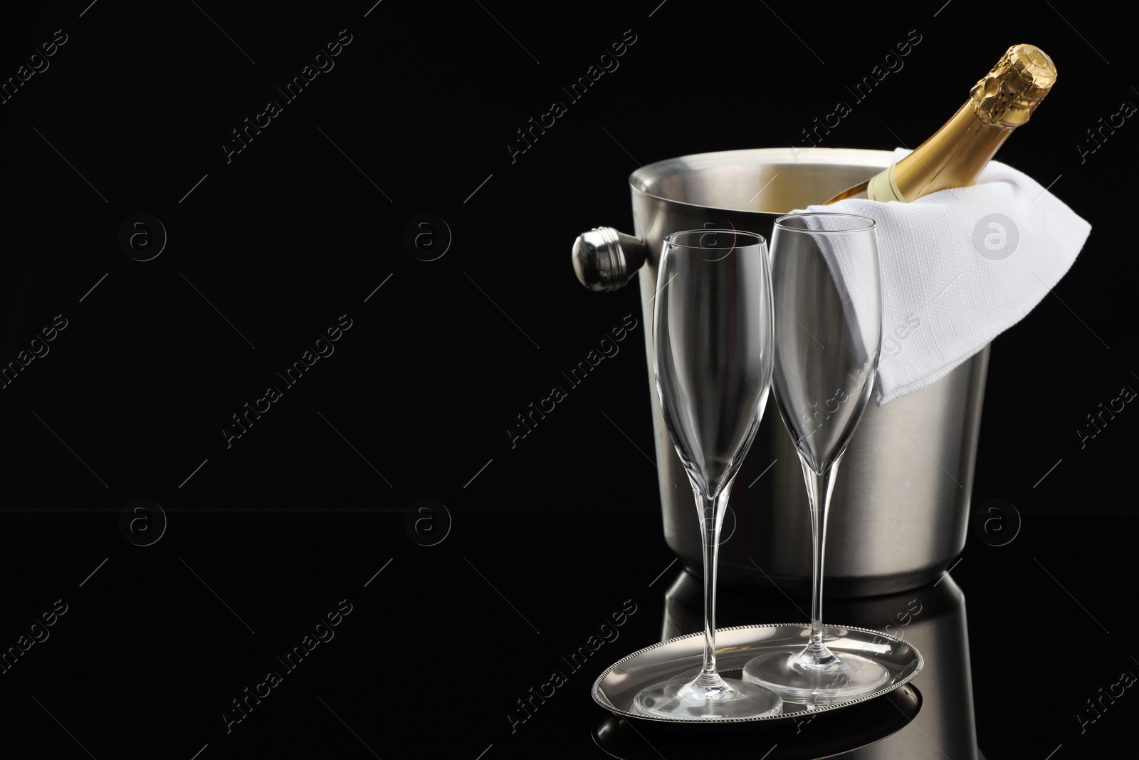 Photo of Bottle of sparkling wine in cooler bucket and glasses against black background. Space for text