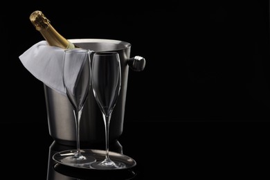 Photo of Bottle of sparkling wine in cooler bucket and glasses against black background. Space for text