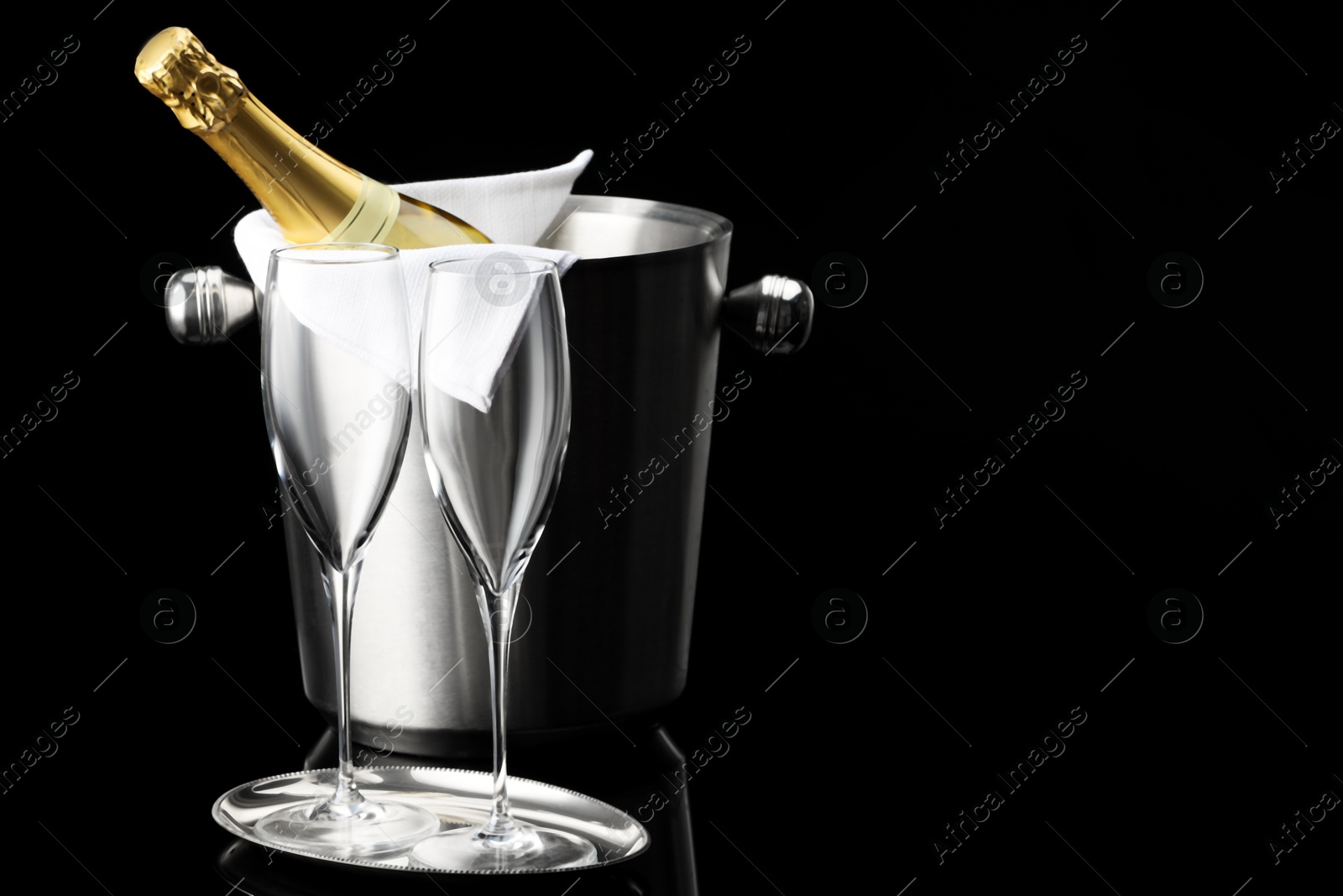 Photo of Bottle of sparkling wine in cooler bucket and glasses against black background. Space for text