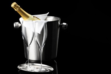 Photo of Bottle of sparkling wine in cooler bucket and glasses against black background. Space for text