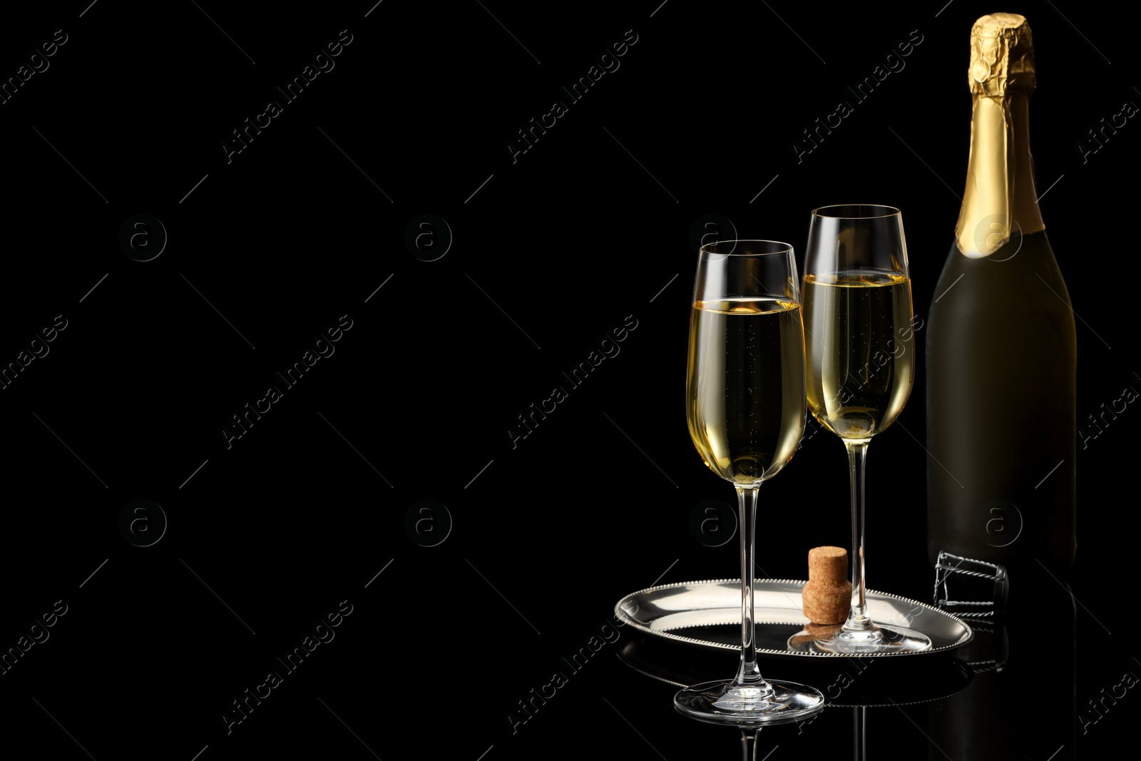 Photo of Bottle and glasses of sparkling wine on black mirror surface. Space for text