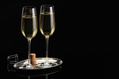 Photo of Glasses of sparkling wine on black mirror surface. Space for text