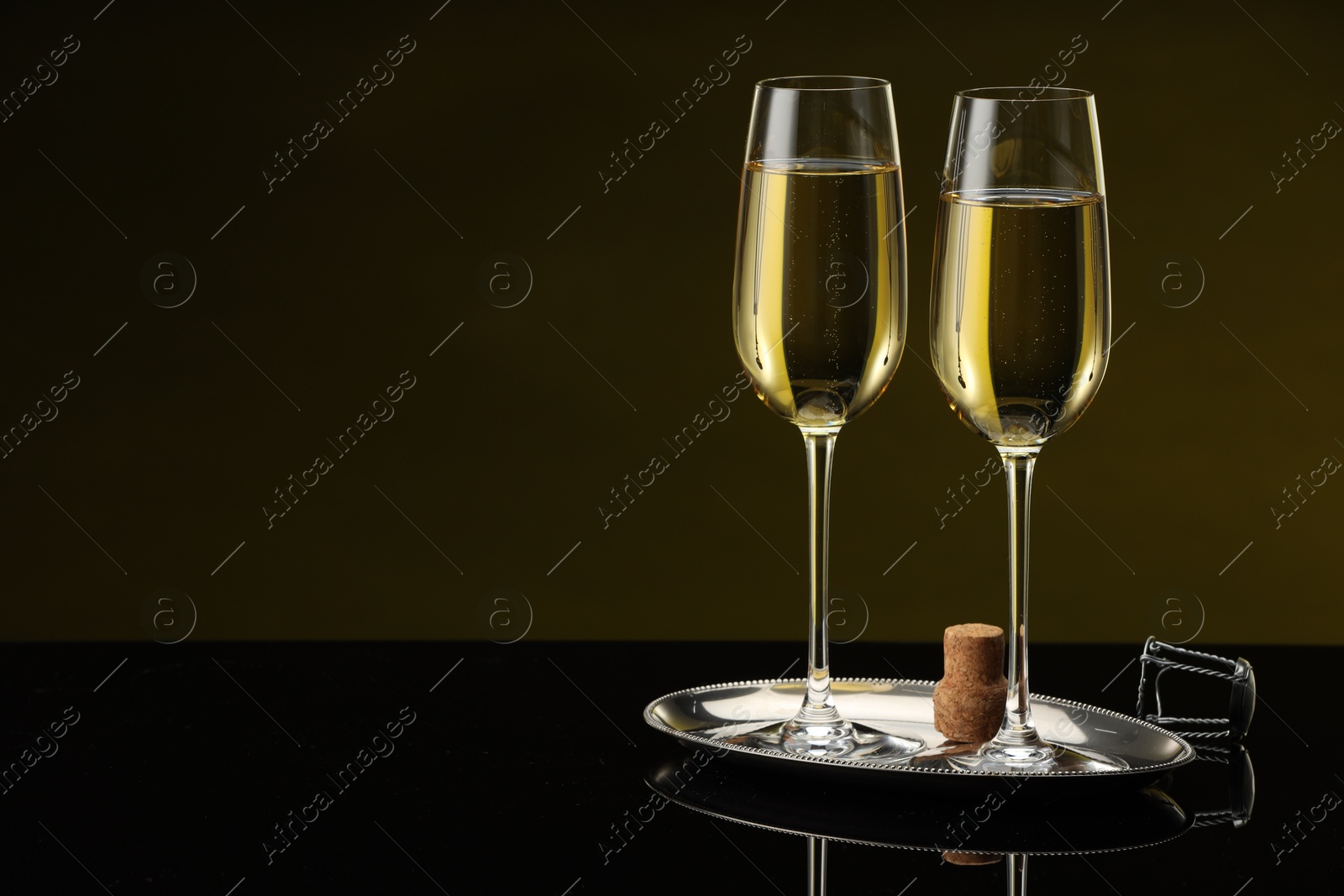 Photo of Glasses of sparkling wine on black mirror surface. Space for text