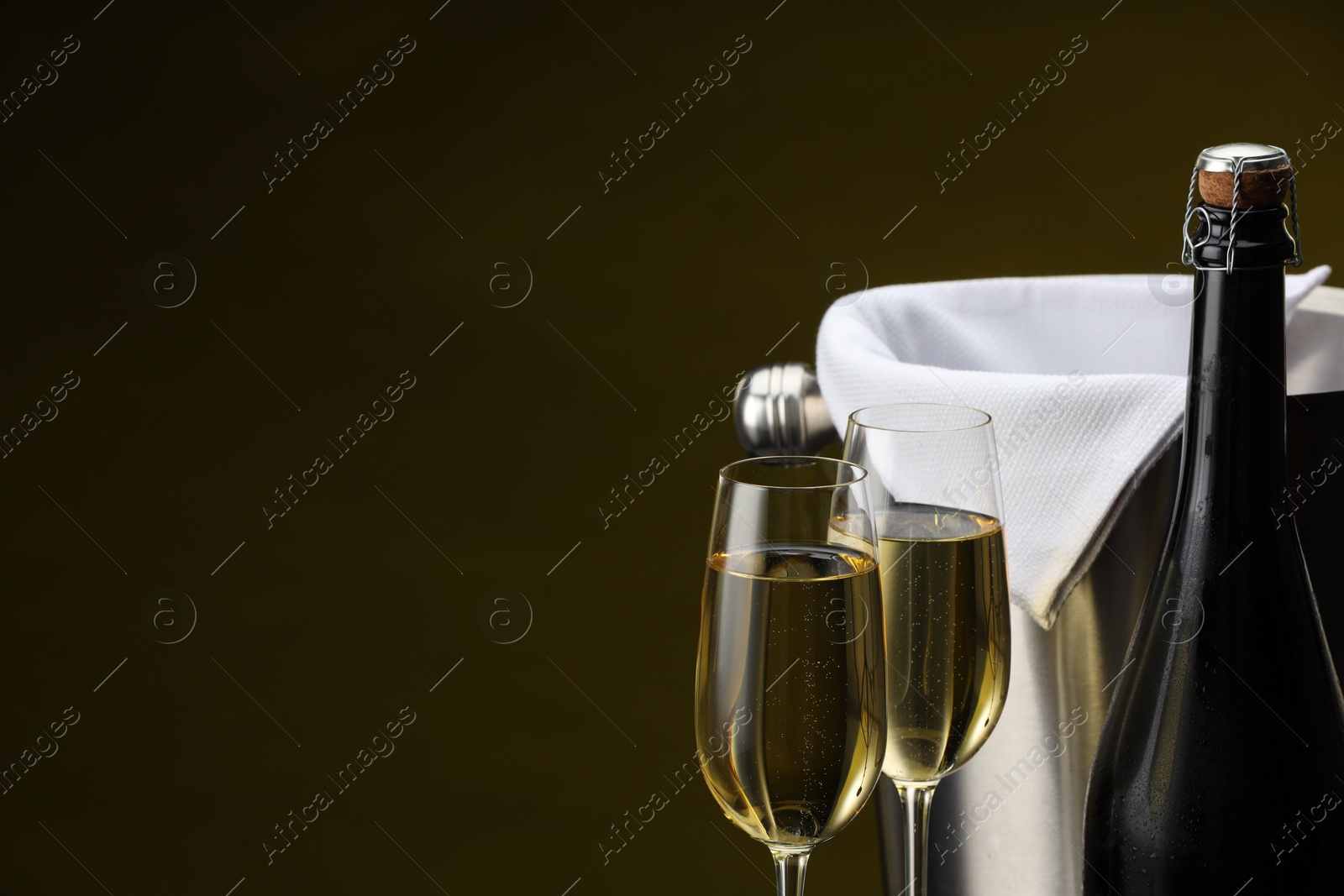 Photo of Bottle of sparkling wine, glasses and cooler bucket on brown background, closeup. Space for text