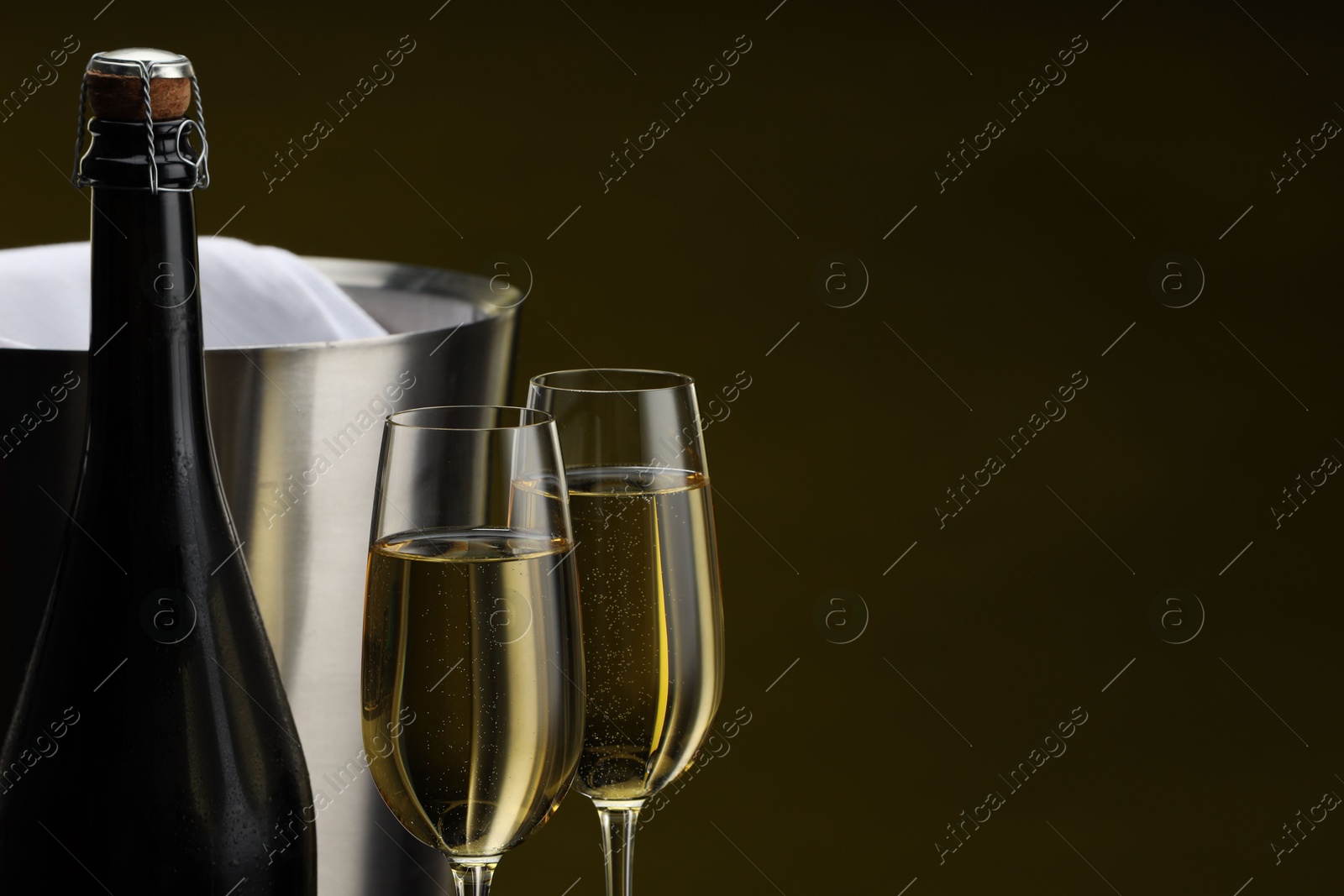 Photo of Bottle of sparkling wine, glasses and cooler bucket on brown background, closeup. Space for text