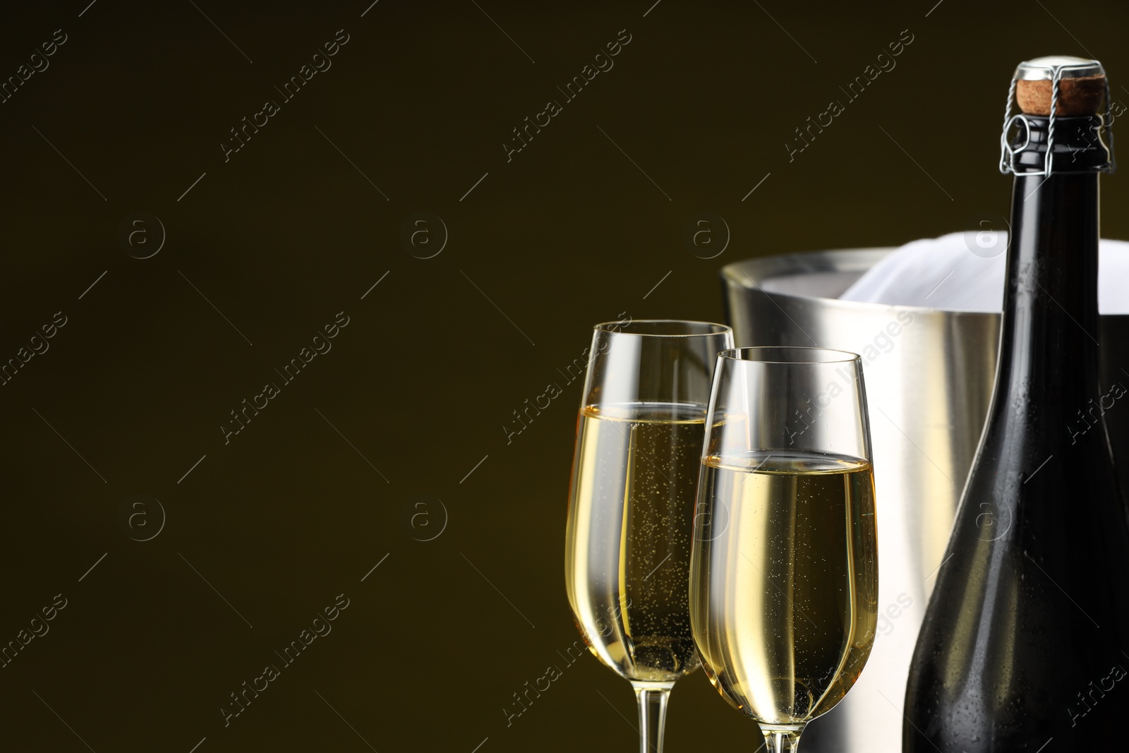 Photo of Bottle of sparkling wine, glasses and cooler bucket on brown background, closeup. Space for text