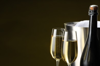 Photo of Bottle of sparkling wine, glasses and cooler bucket on brown background, closeup. Space for text