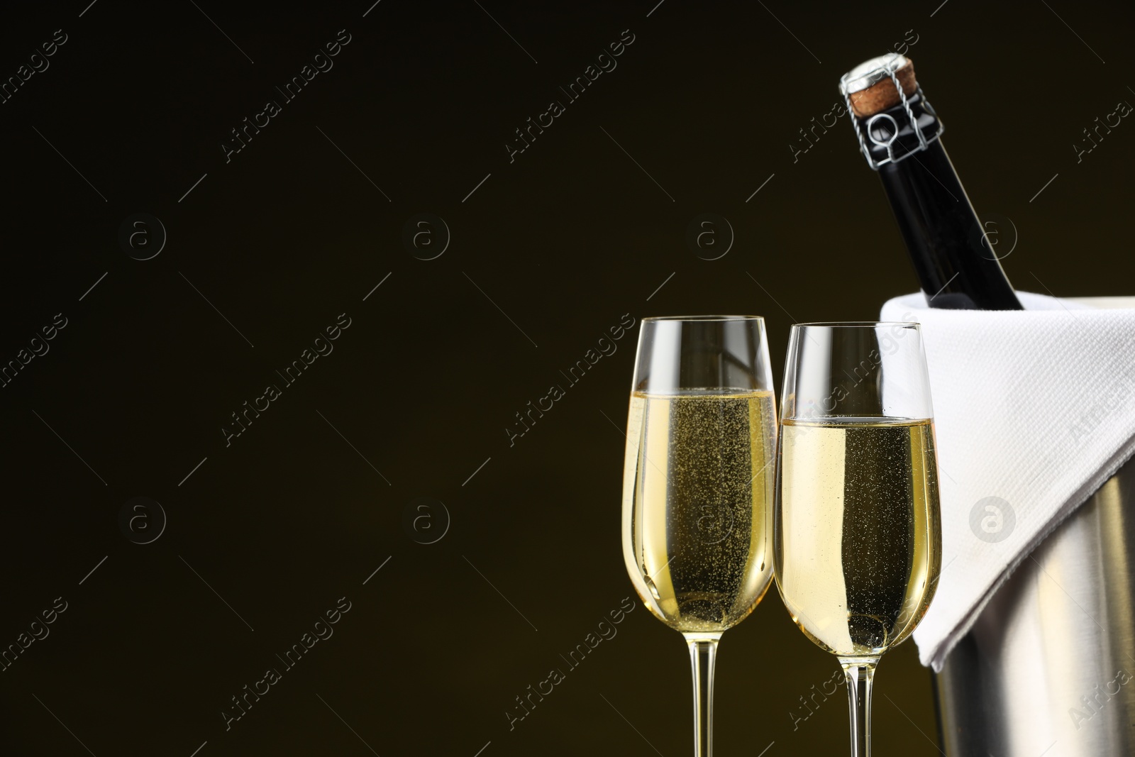 Photo of Bottle of sparkling wine, glasses and cooler bucket on brown background, closeup. Space for text