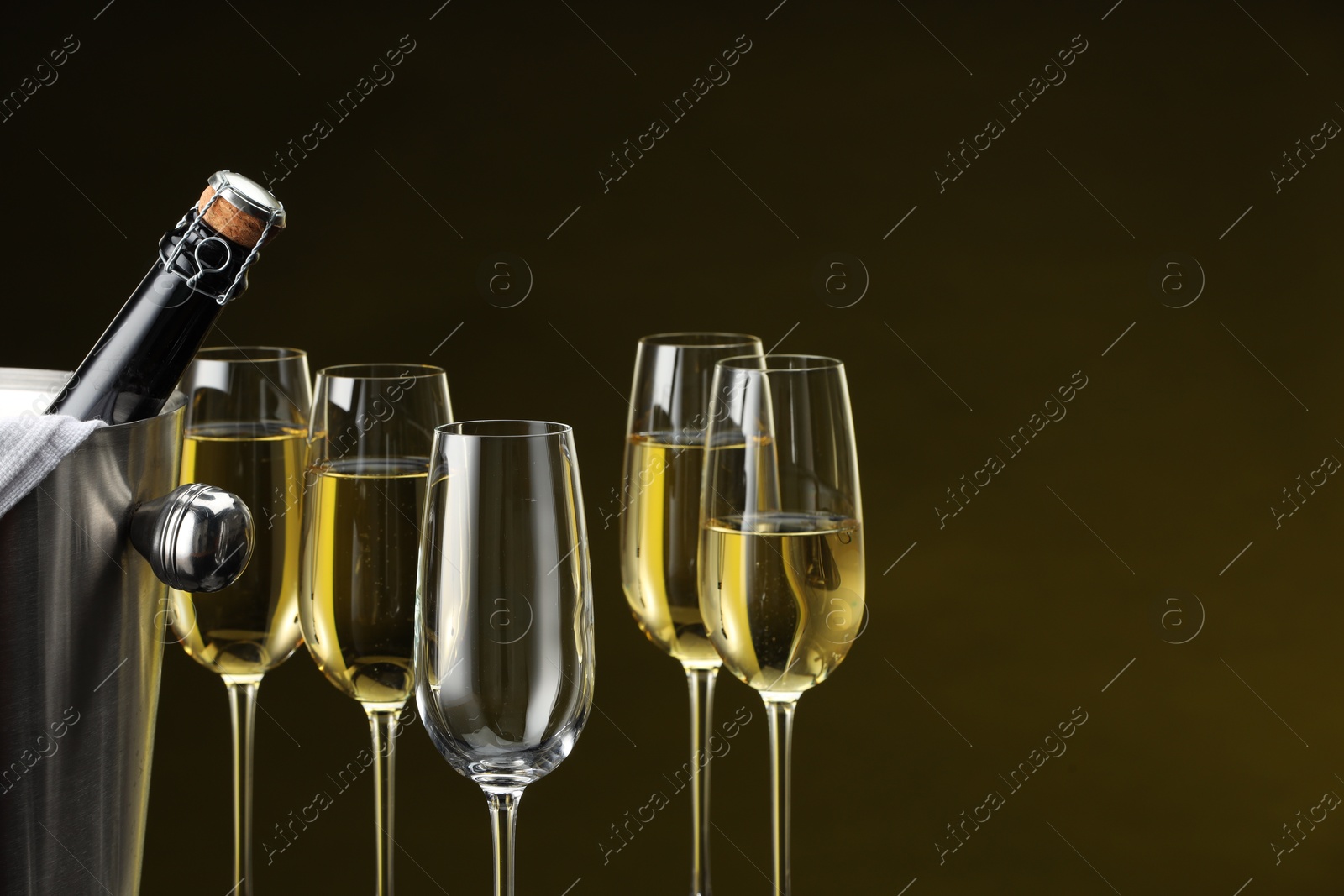 Photo of Bottle of sparkling wine in cooler bucket and glasses against brown background, closeup. Space for text