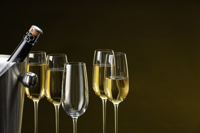 Photo of Bottle of sparkling wine in cooler bucket and glasses against brown background, closeup. Space for text