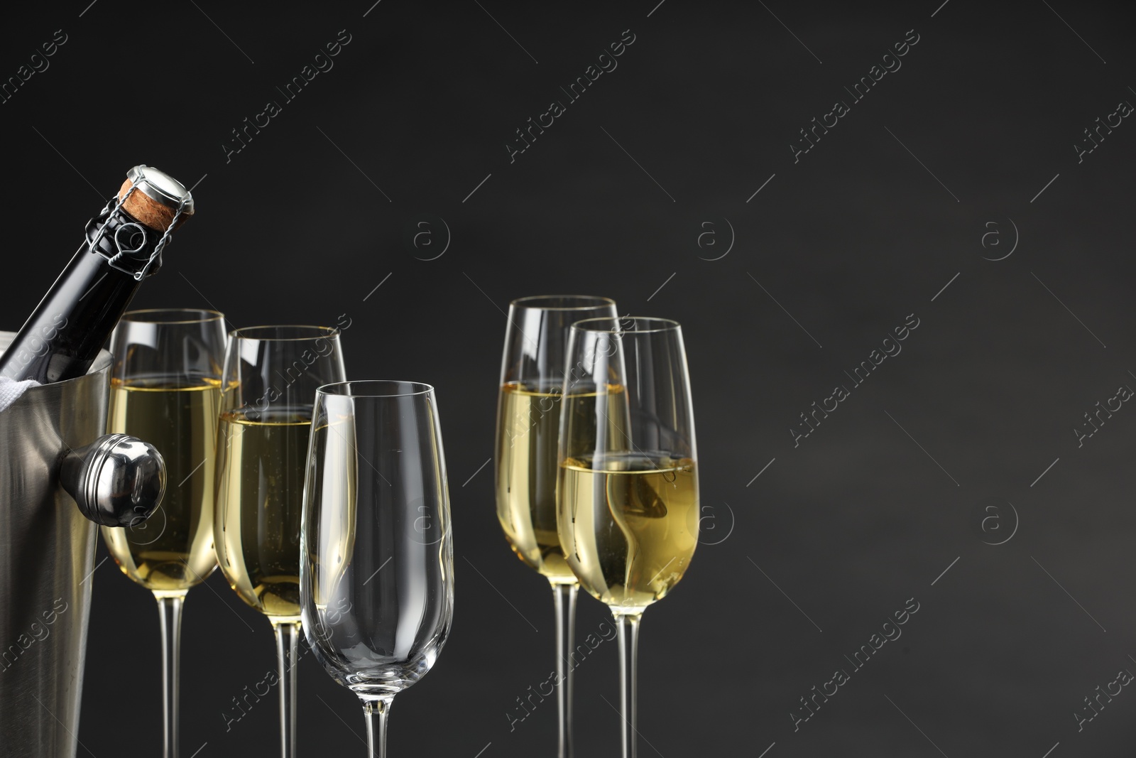 Photo of Bottle of sparkling wine in cooler bucket and glasses against grey background, closeup. Space for text