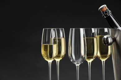 Photo of Bottle of sparkling wine in cooler bucket and glasses against grey background, closeup