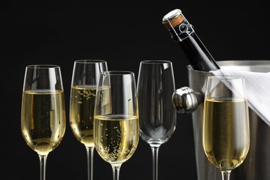 Photo of Bottle of sparkling wine in cooler bucket and glasses against black background, closeup