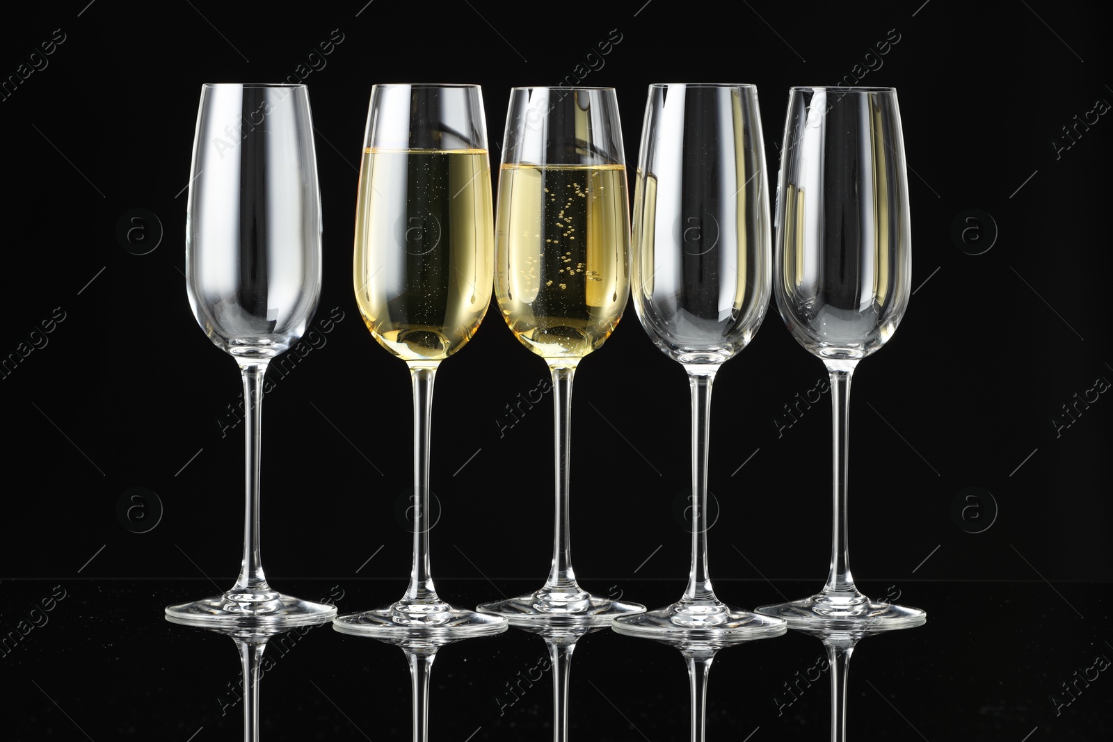 Photo of Glasses of sparkling wine on black mirror surface