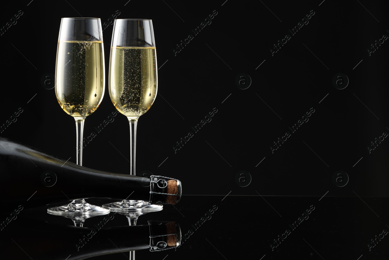 Photo of Bottle and glasses of sparkling wine on black mirror surface. Space for text