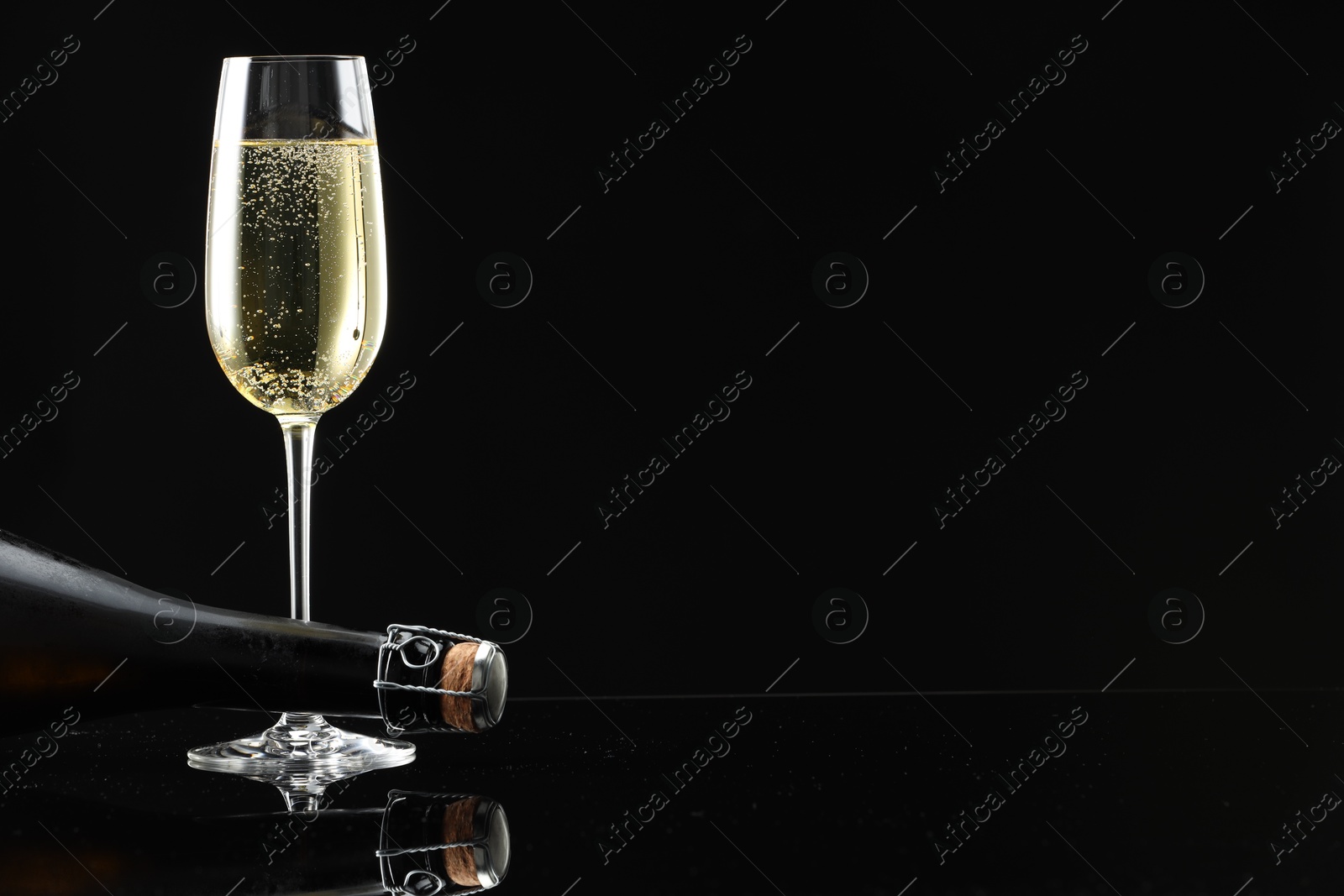 Bottle and glass of sparkling wine on black mirror surface. Space for text Photo of Bottle and glass of sparkling wine on black mirror surface. Space for text