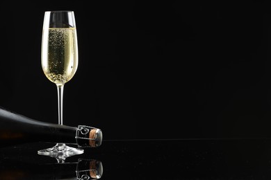 Photo of Bottle and glass of sparkling wine on black mirror surface. Space for text