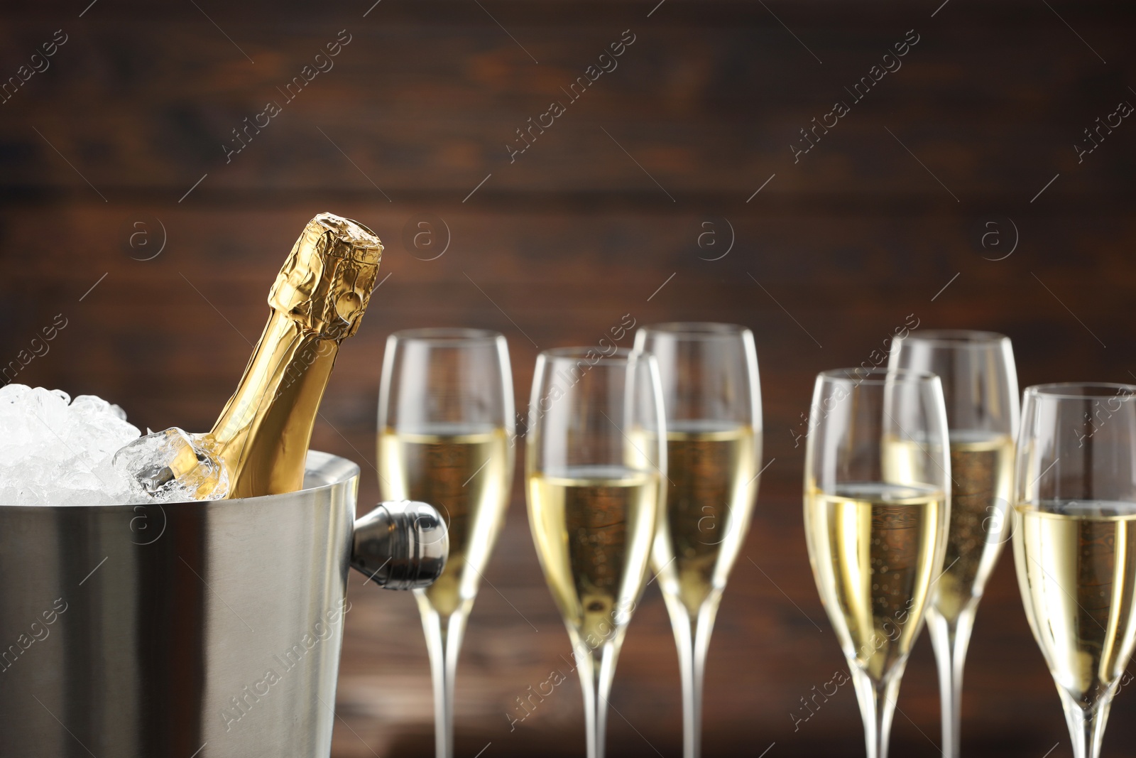 Photo of Bottle of sparkling wine in cooler bucket and glasses against wooden background, closeup