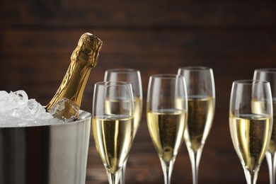 Photo of Bottle of sparkling wine in cooler bucket and glasses against wooden background, closeup