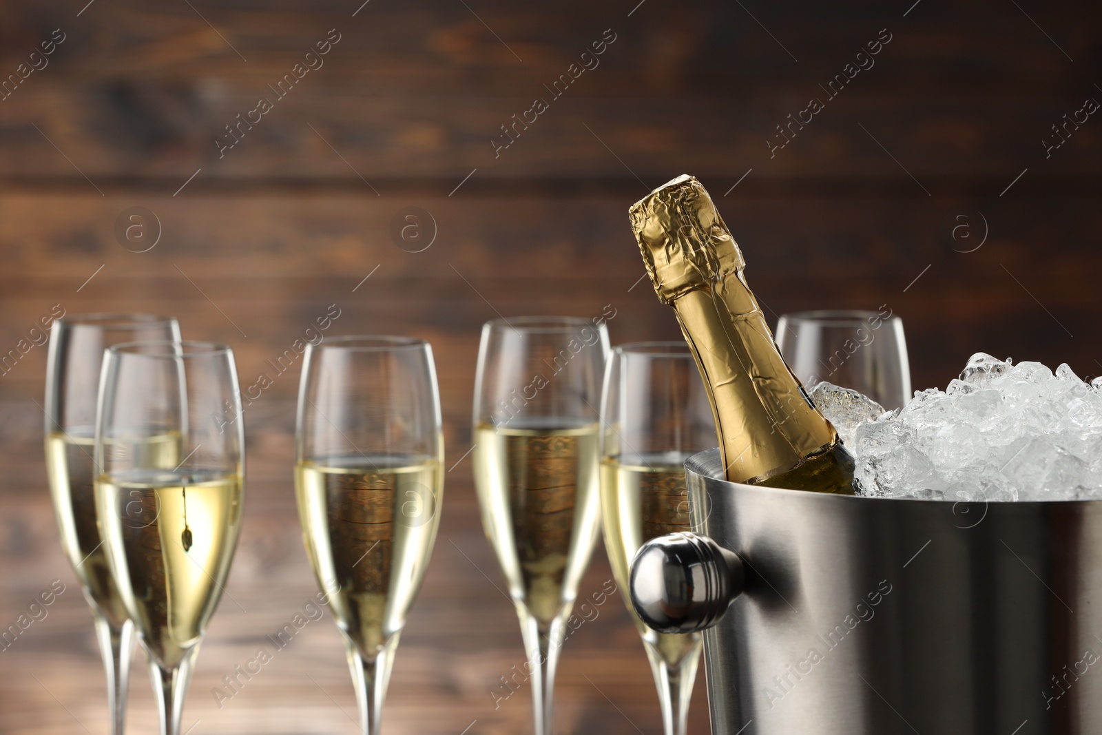 Photo of Bottle of sparkling wine in cooler bucket and glasses against wooden background, closeup