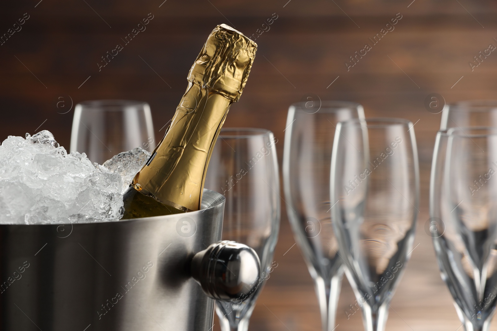 Photo of Bottle of sparkling wine in cooler bucket and glasses against wooden background, closeup