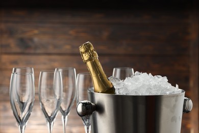 Photo of Bottle of sparkling wine in cooler bucket and glasses against wooden background, closeup