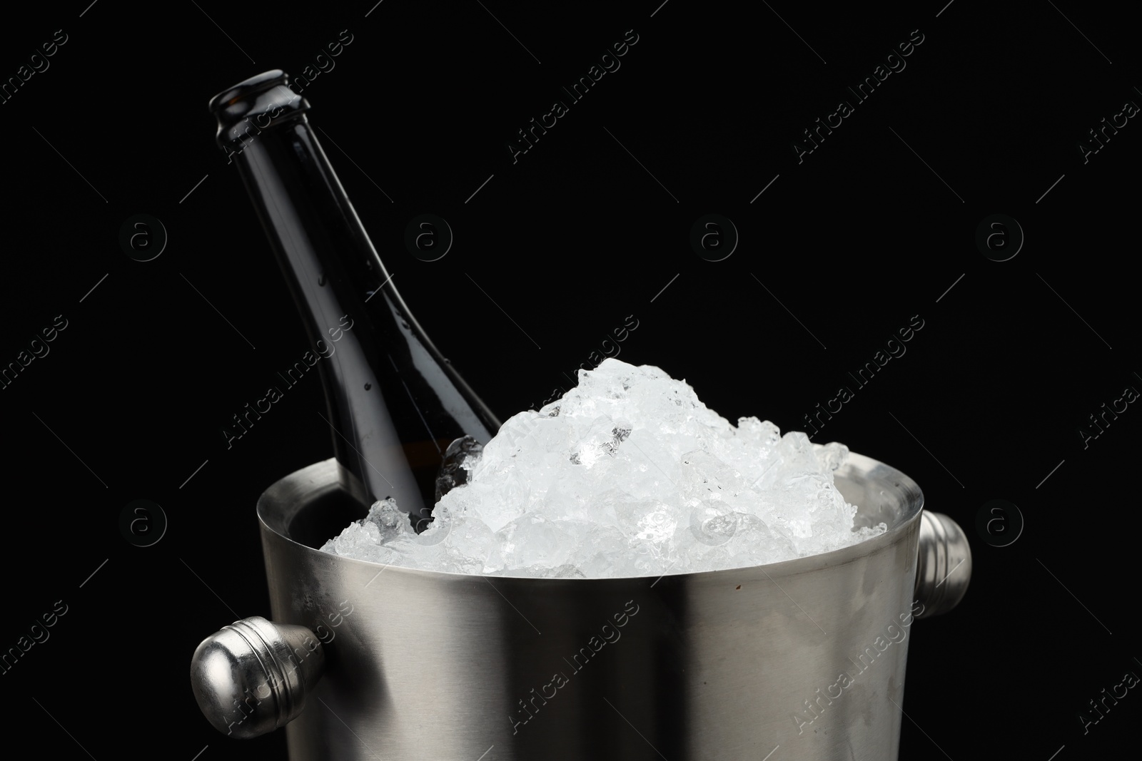 Photo of Bottle of sparkling wine in cooler bucket against black background, closeup. Space for text