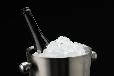 Photo of Bottle of sparkling wine in cooler bucket against black background, closeup. Space for text