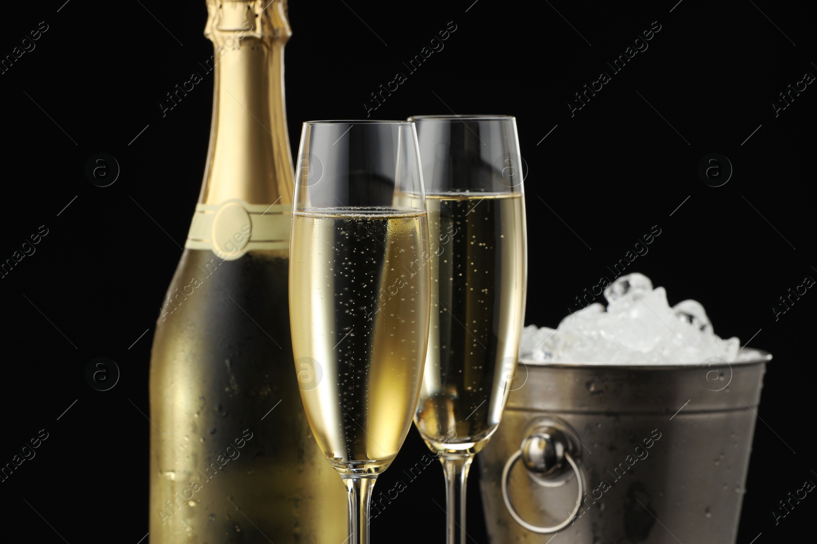 Photo of Bottle of sparkling wine, glasses and cooler bucket on black background, closeup