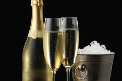 Photo of Bottle of sparkling wine, glasses and cooler bucket on black background, closeup