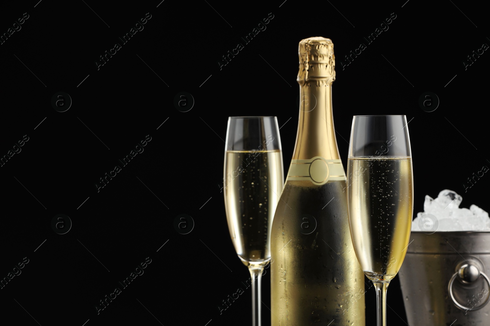 Photo of Bottle of sparkling wine, glasses and cooler bucket on black background, closeup. Space for text