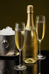 Photo of Bottle of sparkling wine, glasses and cooler bucket on black mirror surface