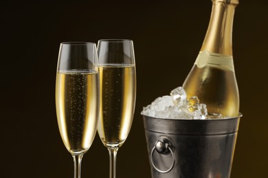 Bottle of sparkling wine in cooler bucket and glasses against brown background, closeup